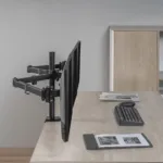 מערך משרד ביתי מינימליסטי עם זרוע שולחנית דו מפרקית ל3 מסכי מחשב עד "27 מחזיק מסך אחד, מקלדת, עכבר ומחברת על שולחן עץ.