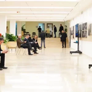 יחידים במסדרון עם יצירות אמנות, חלקם יושבים ואחרים עומדים.