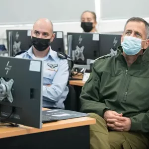 שני אנשים עוטים מסכות יושבים ליד מחשבים בחדר עם אחרים, ככל הנראה עוסקים בסביבת הכשרה או עבודה.